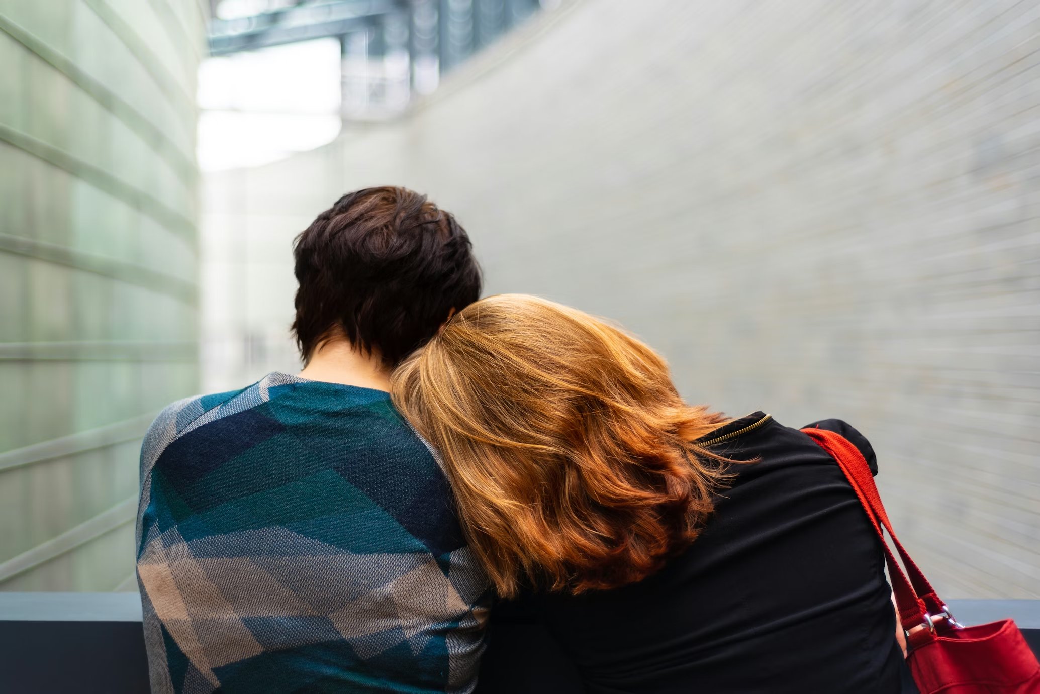 Two people sitting together, one resting their head on the other's shoulder in a moment of quiet comfort and support.